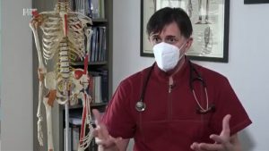 Dr. Šime Mijić s maskom i stetoskopom govori pokraj modela kralježnice